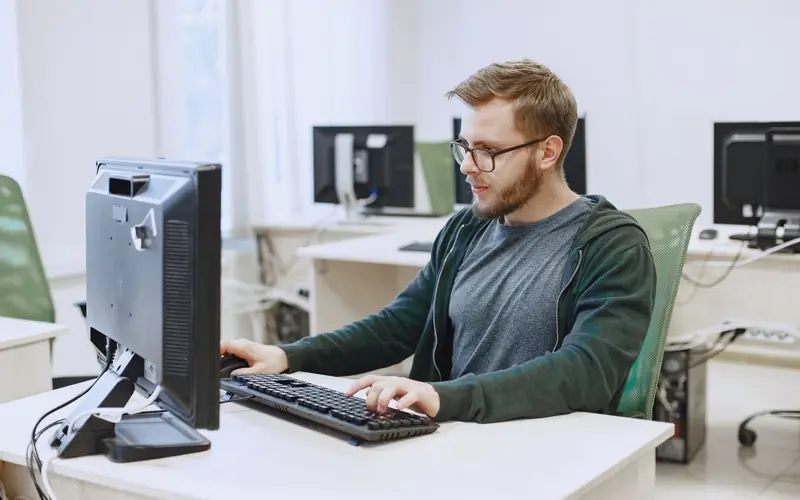 IT administrator in glasses working at a desktop computer in a bright office